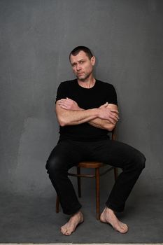 Calm men sits on a chair. Vertical photo on a gray background