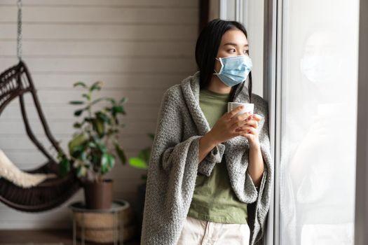 Asian girl in medical face mask, yearning go outside, being sick with covid 19 and staying on self quarantine in her house.