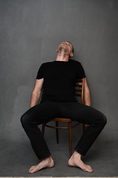 A full-length man sits on a chair with his head up. Vertical photo on a gray background