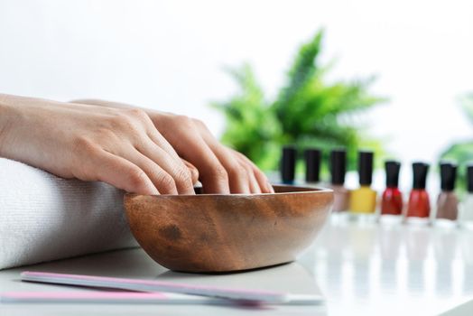 Closeup female hands in wooden bowl with water. Spa procedure and relaxation. Female hands preparing for manicure. Professional nail care and beautician service. Beauty and hygiene concept