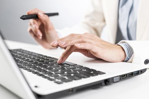 Man in business suit sitting at desk and working at laptop computer. Close-up of male hands typing on laptop keyboard. Businessman at workplace in office. Business innovation and digital technology