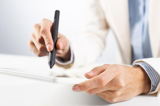 Man in business suit using tablet computer. Close-up of male hands holding pen and tablet gadget. Businessman at workplace in office. Mobile smart device in business occupation. Digital technology