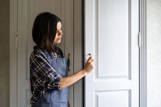 A young girl in casual clothes opens the door of a white wooden cabinet in her light, cozy room.