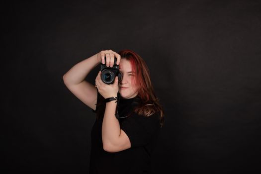 redhead girl with a professional camera posing on black background. woman female photographer