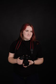 redhead girl with a professional camera posing on black background. woman female photographer