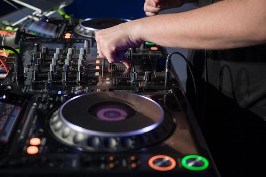 Close-Up of Dj Mixer Controller Desk in Night Club Disco Party. DJ Hands touching Buttons and Sliders Playing Electronic Music . High quality photography.