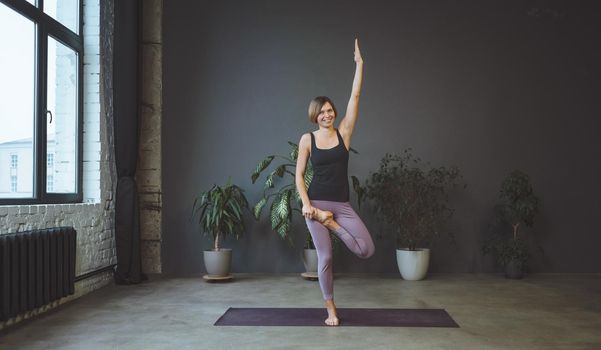 Lonely Woman in Sportswear Doing Side Plank in a Spacious Yoga Studio. Sporty Fit Woman Practices Hatha Yoga. Full Length. Gray Background. High quality photo