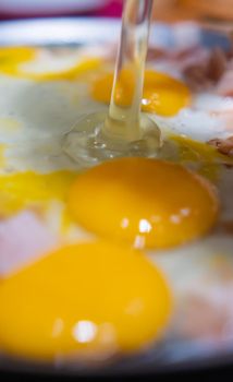Extreme close-up of chopped turkey ham and three raw egg yolks on a round griddle. Cooking thin turkey breast meat and scrambled eggs on frying pan. Healthy meal preparation
