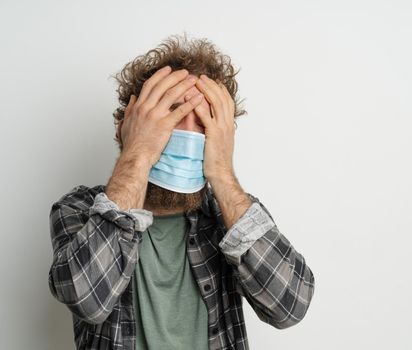 Caucasian Man in a Medical Mask has a Headache, Symptoms of Illness, Feeling Unwell, Malaise. White background. Close-up. Copy Space. High quality photo