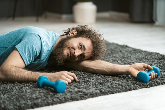 Sly Lazy Guy Lies on the Floor with Small Dumbbells in his Hands, Pretending to be Tired. Sport at Home. Copy Space. Close-up. High quality photo