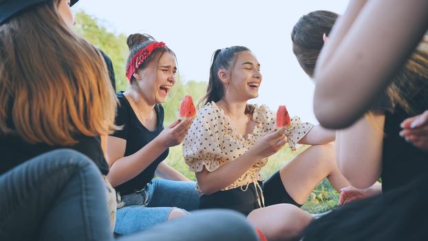 Friends have fun eating watermelon outside the city at a picnic