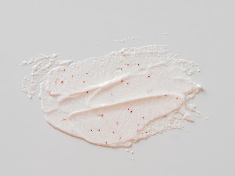 Scrub smears isolated on white background. Texture cosmetic scrub for face and body with red abrasive particles in pastel pink color. Exfoliating body polish texture as cosmetic gommage background with copy space