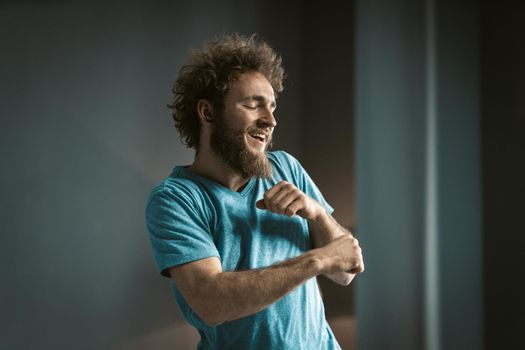 Coily Guy in a Blue T-shirt and a Tattoo on his Neck Makes Funny Movements by his Hands. Young Man Dancing in the Room at Home.Copy Space. Close-up. High quality photo