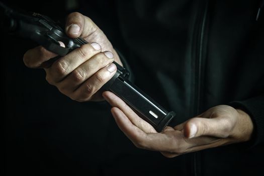 Reloading gun close-up. Man inserts drum of cartridges into pistol. Firearms in hand on dark background. Defense or attack.