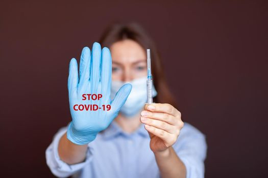 Coronavirus concept. Girl wearing mask for protection from disease and show stop hands gesture for stop corona virus outbreak. Stop the pandemic with vaccination. There is a syringe in the girl's hand