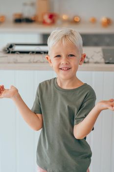 Happy little boy with blond hair is standing and ready to bake a Christmas cookies at home. Kid smiling and having fun during the Christmas holidays. Concept of preparation for Christmas Eve.