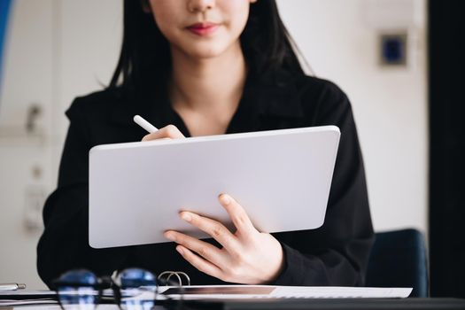 Electronic work concept, female employee is using tablet and ducument to analyze company profits to improve revenue over last year