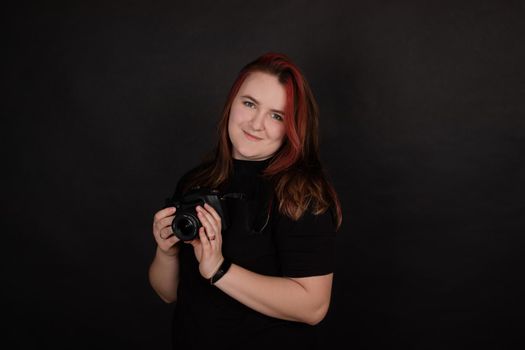 redhead girl with a professional camera posing on black background. woman female photographer