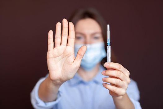 Coronavirus concept. Girl wearing mask for protection from disease and show stop hands gesture for stop corona virus outbreak. Stop the pandemic with vaccination. There is a syringe in the girl's hand