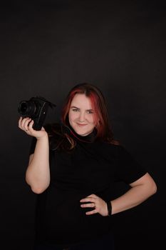 redhead girl with a professional camera posing on black background. woman female photographer