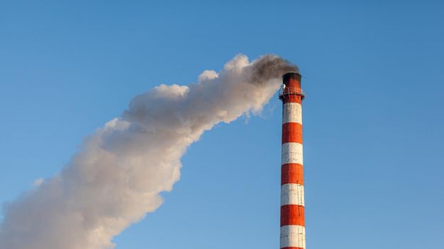 White thick smoke from the boiler room chimney. Smoke against the blue sky. Air pollution. Heating of the city. Industrial zone.