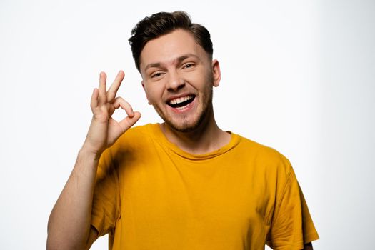 Cheerful Guy in a Yellow T-shirt Shows a Gesture of Okey on a White Background in the Studio. Positive Gesture, Ok Gesture. Copy Space. Close-up. High quality photo