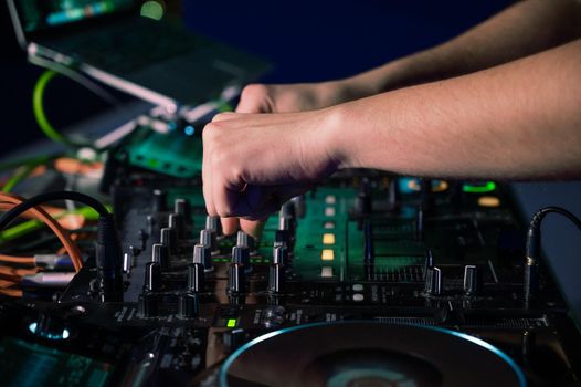 Close-Up of Dj Mixer Controller Desk in Night Club Disco Party. DJ Hands touching Buttons and Sliders Playing Electronic Music . High quality photography.