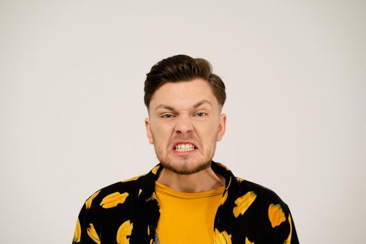 Negative Emotion to the Camera. Man in a Yellow T-shirt and a Funny Shirt on a White Background in the Studio. Angry Guy. Copy Space. Close-up. High quality photo