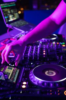 Close-Up of Dj Mixer Controller Desk in Night Club Disco Party. DJ Hands touching Buttons and Sliders Playing Electronic Music . High quality photography.