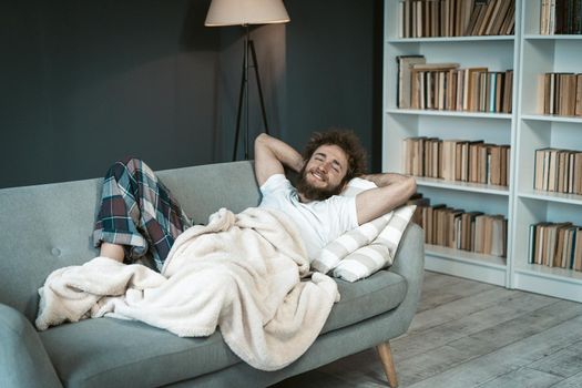 Young Man in Pajamas Enjoying Relaxing on the Couch. Cute Guy has a Rest on the Sofa in his Living Room at Home. Time to Sleep. Close-up. Copy Space. High quality photo