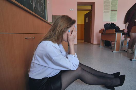 Pupils run to calm down their friend who is crying on the floor in the classroom