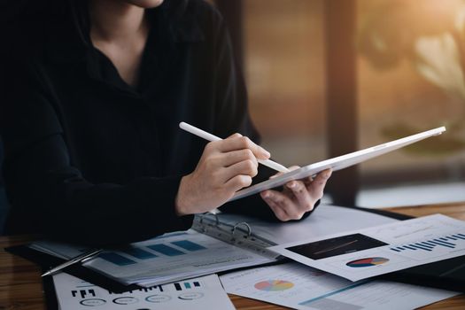 Electronic work concept, female employee is using tablet and ducument to analyze company profits to improve revenue over last year