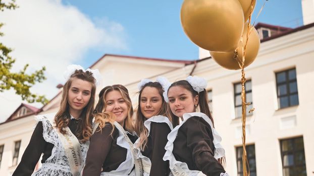 Cheerful Russian girls graduating with orange balloons on the last school day