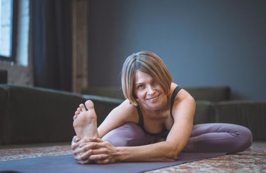 Smiling young woman on a mat does an asana. Concept of yoga in the city. Health, longevity, slim figure. High quality photo