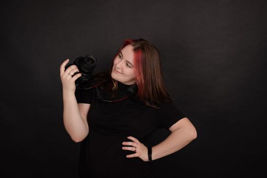 redhead girl with a professional camera posing on black background. woman female photographer