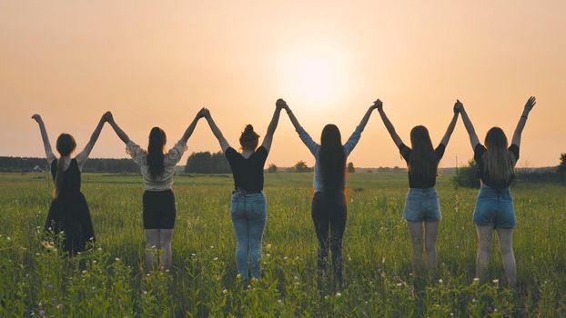 Girls friends raise their hands at sunset