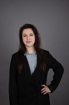 attractive confident brunette business woman in blue blouse and black jacket on grey background.