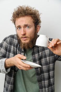 Surprised Man Holding White Empty Cup Upside Down and Saucer. Empty Coffee Cup. White Background. Close-up. Copy Space. High quality photo