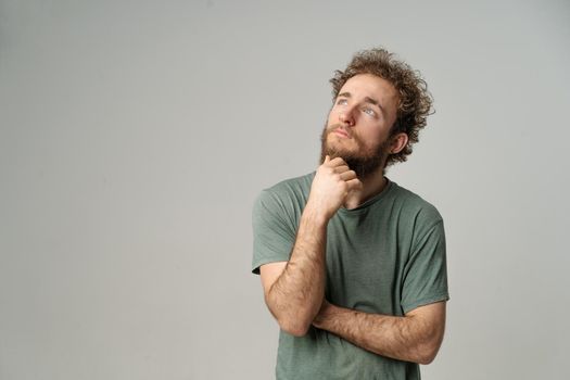 Dreamy Curly Guy Looks to the Copy Space ,Thoughtful Man Thinks about his Future. Male Model in Graphite T-shirt Posing in Studio with Light Gray Background. Close-up. High quality photo