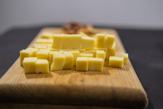 Close-up of diced yellow cheese and walnuts on cutting board. Wooden board with fresh cheese cubes and nuts above black surface. Healthy snacks and balanced diet