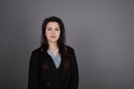 attractive confident brunette business woman in blue blouse and black jacket on grey background.