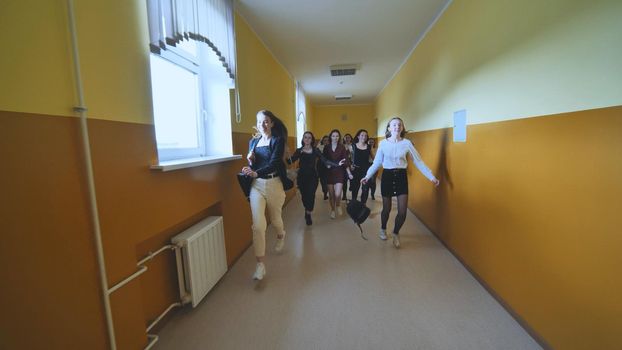Joyful schoolgirls run after the end of the lessons in the school corridor