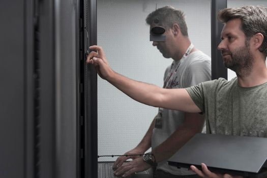 A couple of server engineers cooperate in high tech data centers. Technicians team updating hardware inspecting system performance in super computer server room or cryptocurrency mining farm.