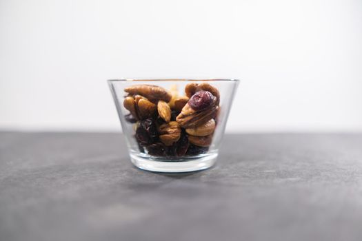 Close-up of small glass of walnuts, almonds, Indian nuts, and dry cranberries with black and white background. Fresh natural nuts in glass cup above dark surface. Tasty traditional snacks