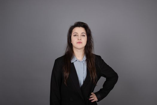 attractive confident brunette business woman in blue blouse and black jacket on grey background.