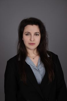 attractive confident brunette business woman in blue blouse and black jacket on grey background.