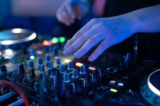 Close-Up of Dj Mixer Controller Desk in Night Club Disco Party. DJ Hands touching Buttons and Sliders Playing Electronic Music . High quality photography.