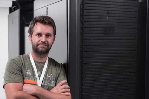 Portrait of male technician or network administrator standing brave as a hero with arms crossed in data center server room. High quality photo