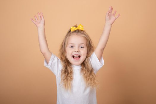 portrait of a sweet blonde little girl in white t-shirt and with yellow bow on her head. on brown background.