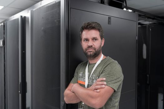 Portrait of male technician or network administrator standing brave as a hero with arms crossed in data center server room. High quality photo